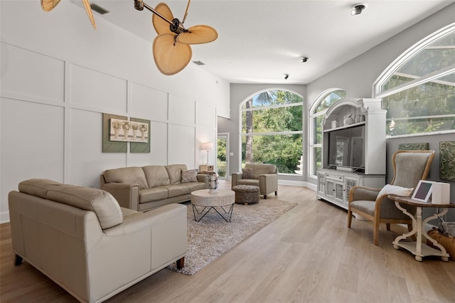 living room with ceiling fan, a high ceiling, and light wood-type flooring