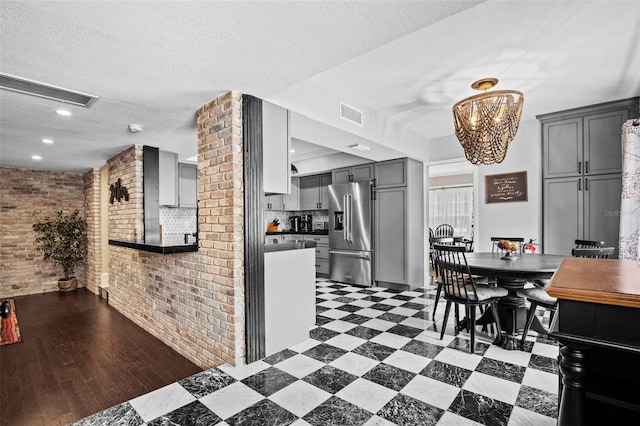 kitchen with gray cabinets, brick wall, high end fridge, and a notable chandelier