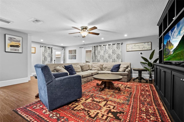 living room featuring ceiling fan, dark wood-type flooring, and a textured ceiling