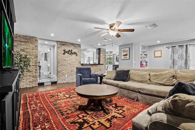 living room with ceiling fan, brick wall, dark hardwood / wood-style floors, and a textured ceiling