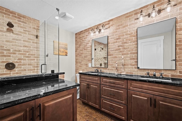 bathroom with vanity, walk in shower, a textured ceiling, and brick wall