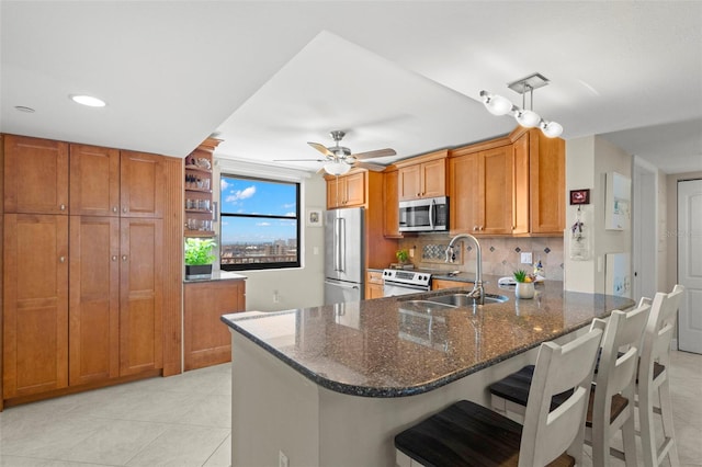 kitchen with sink, light tile patterned floors, stainless steel appliances, kitchen peninsula, and dark stone counters