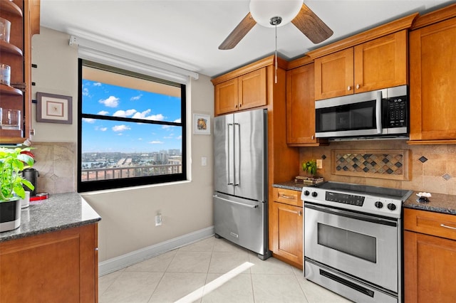 kitchen featuring light tile patterned floors, ceiling fan, appliances with stainless steel finishes, tasteful backsplash, and dark stone counters