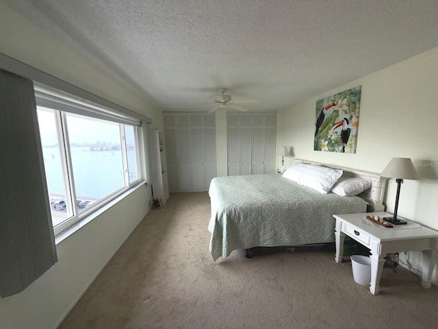 carpeted bedroom featuring multiple closets, a water view, a textured ceiling, and ceiling fan