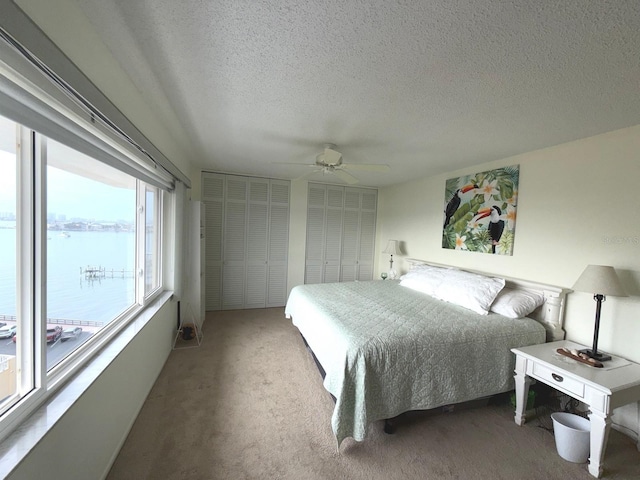 bedroom with a water view, carpet flooring, a textured ceiling, and ceiling fan