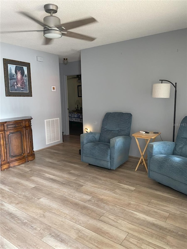 living area with ceiling fan, a textured ceiling, and light hardwood / wood-style flooring