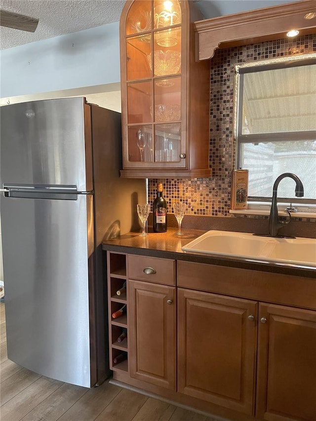 bar with stainless steel fridge, light hardwood / wood-style floors, sink, and backsplash