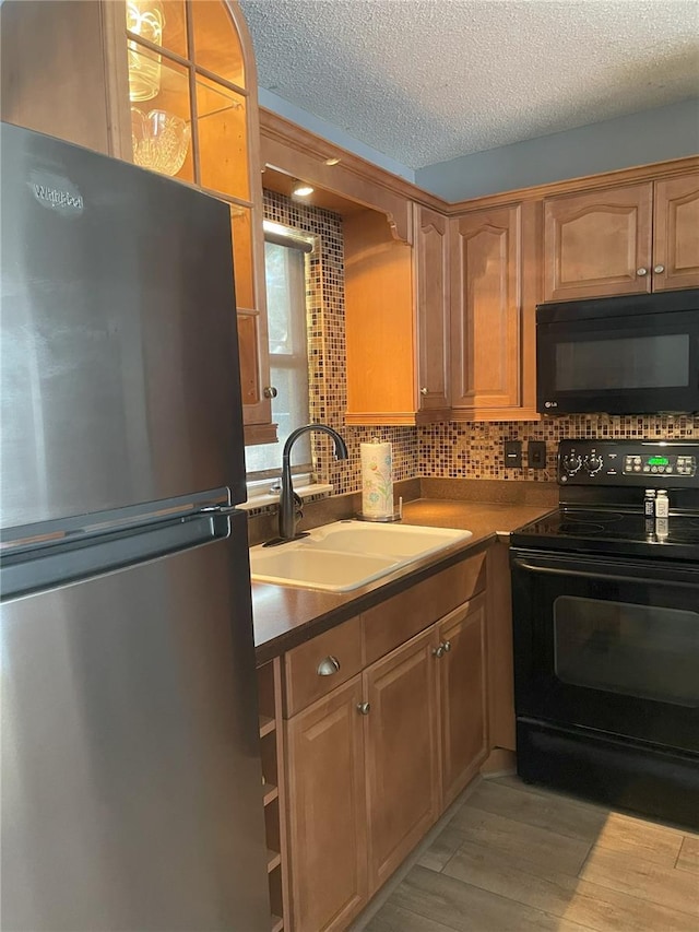 kitchen with sink, tasteful backsplash, black appliances, light hardwood / wood-style floors, and a textured ceiling