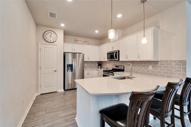 kitchen with pendant lighting, sink, appliances with stainless steel finishes, white cabinetry, and tasteful backsplash