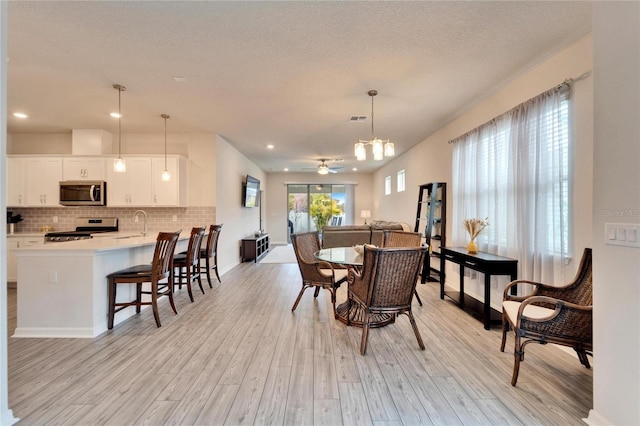 dining space featuring light wood finished floors, visible vents, ceiling fan, a textured ceiling, and baseboards