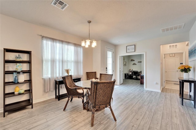 dining space featuring light wood finished floors, visible vents, and an inviting chandelier