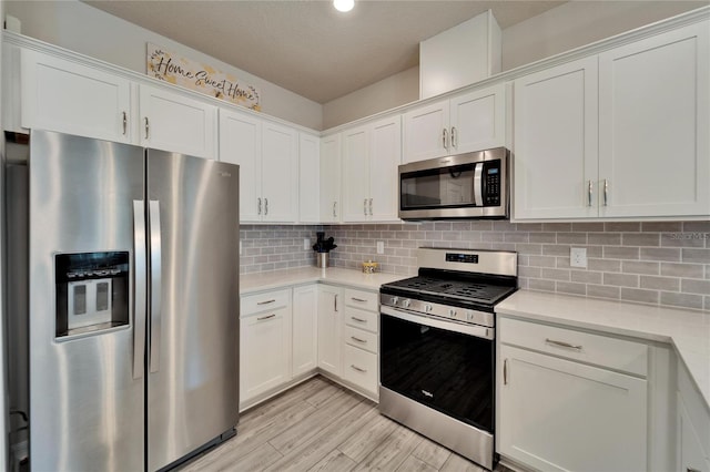 kitchen featuring light countertops, decorative backsplash, appliances with stainless steel finishes, white cabinetry, and light wood-type flooring