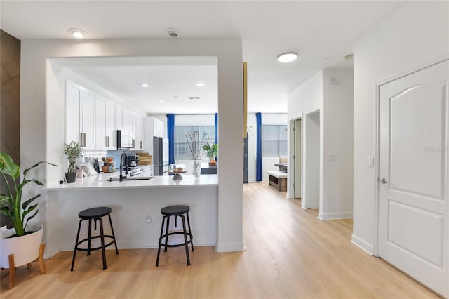 kitchen with a breakfast bar, sink, white cabinets, kitchen peninsula, and light hardwood / wood-style flooring