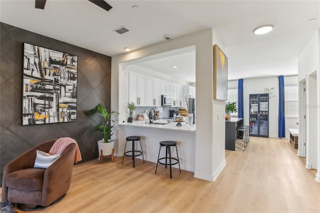 kitchen featuring tasteful backsplash, white cabinets, light hardwood / wood-style floors, and kitchen peninsula