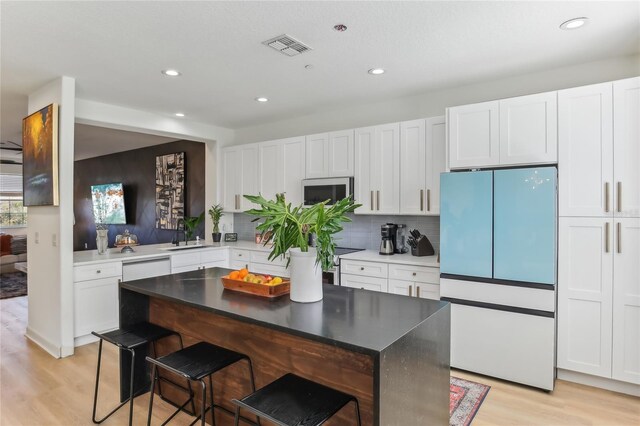 kitchen with a breakfast bar, white cabinets, white appliances, and light hardwood / wood-style flooring