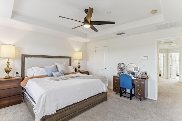 bedroom with ceiling fan, light colored carpet, and a tray ceiling