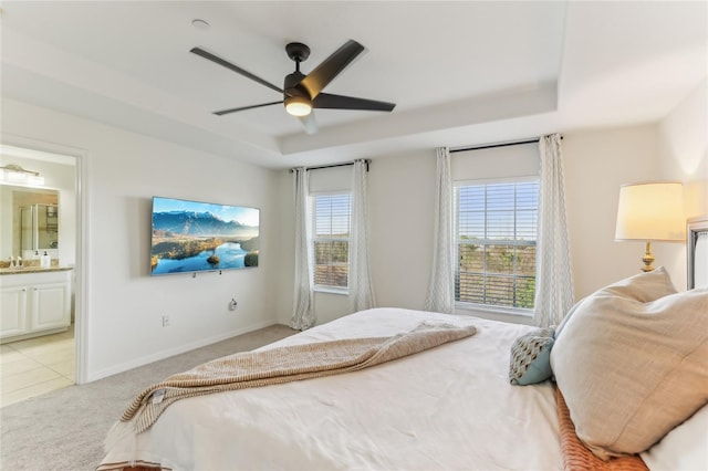 bedroom with a raised ceiling, ceiling fan, light carpet, and ensuite bath