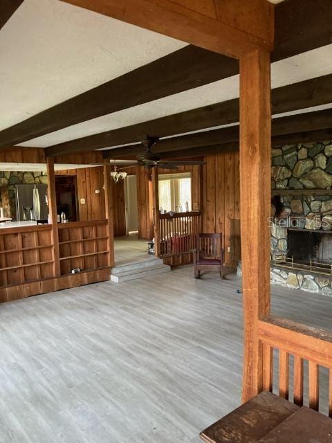 interior space with a fireplace, wooden walls, wood-type flooring, stainless steel refrigerator with ice dispenser, and beam ceiling