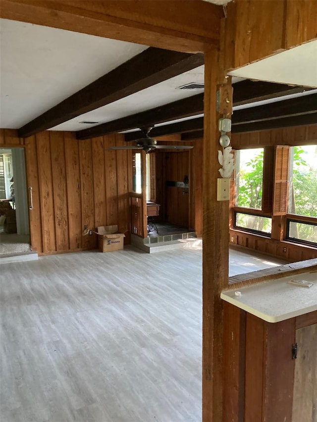 unfurnished living room featuring wood walls, beam ceiling, and light hardwood / wood-style floors