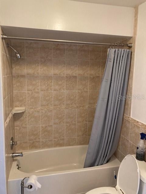 bathroom with tile walls, shower / bath combination with curtain, and toilet