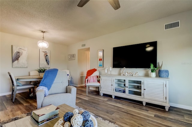 living room with hardwood / wood-style flooring, ceiling fan, and a textured ceiling