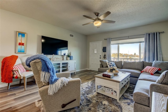 living room featuring hardwood / wood-style flooring, ceiling fan, and a textured ceiling