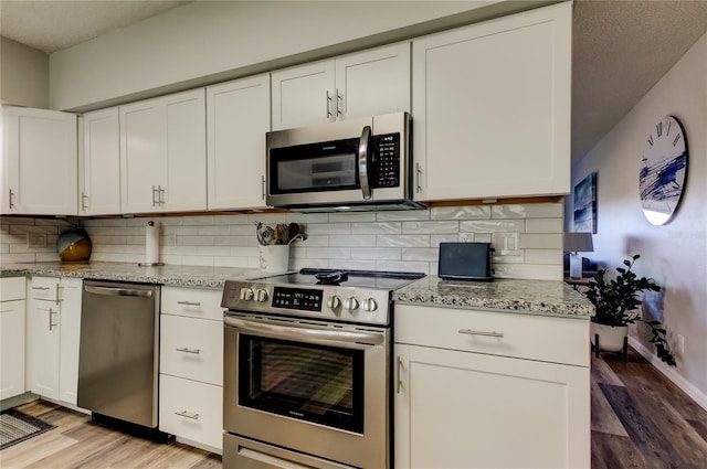 kitchen featuring white cabinetry, backsplash, light stone countertops, and appliances with stainless steel finishes