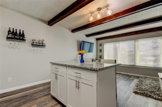 kitchen featuring beamed ceiling, white cabinetry, light stone counters, dark wood-type flooring, and a textured ceiling