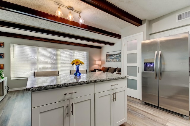 kitchen featuring white cabinetry, light stone counters, a textured ceiling, stainless steel fridge with ice dispenser, and beamed ceiling