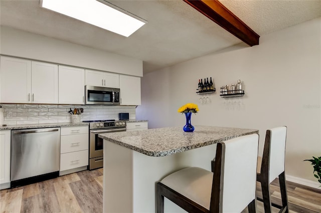 kitchen featuring stainless steel appliances, white cabinetry, and light stone countertops