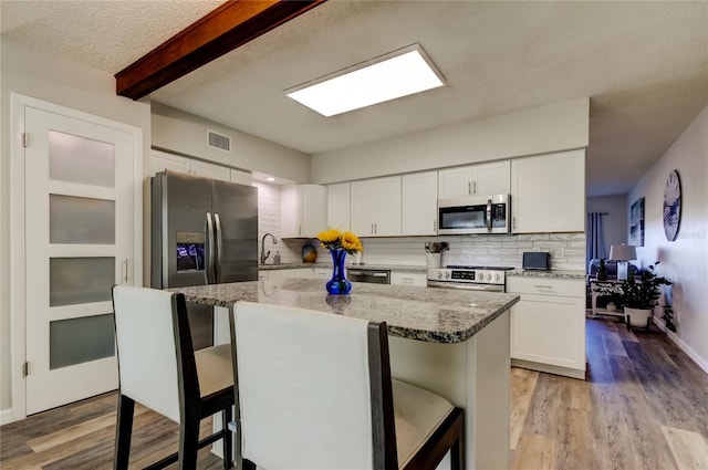 kitchen with white cabinetry, light stone counters, stainless steel appliances, and a kitchen breakfast bar