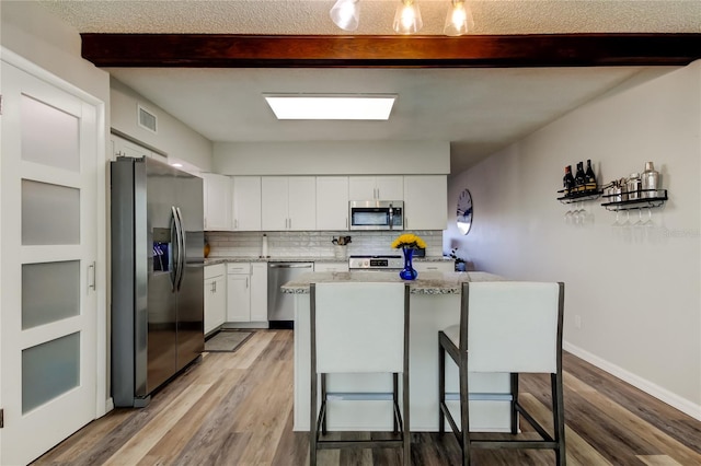 kitchen featuring appliances with stainless steel finishes, backsplash, white cabinets, a kitchen bar, and beamed ceiling