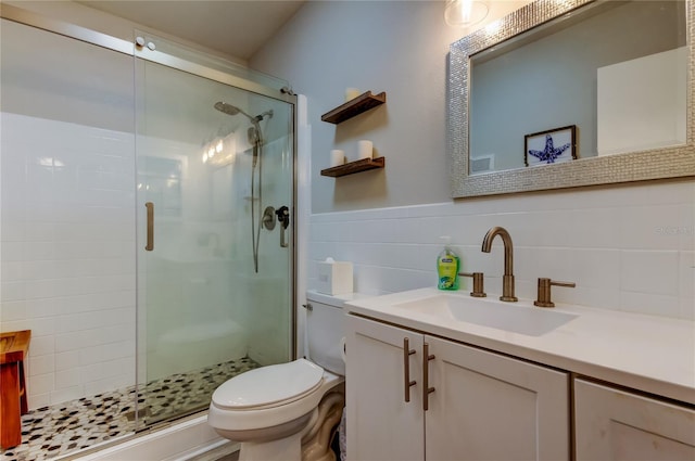 bathroom with vanity, a shower with shower door, tile walls, and toilet