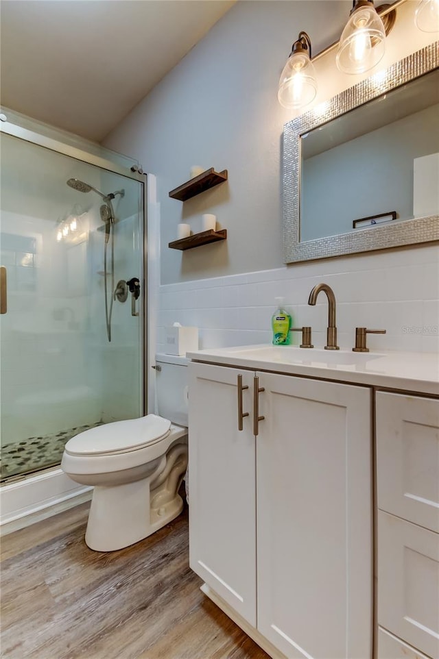 bathroom featuring wood-type flooring, tile walls, vanity, toilet, and a shower with door