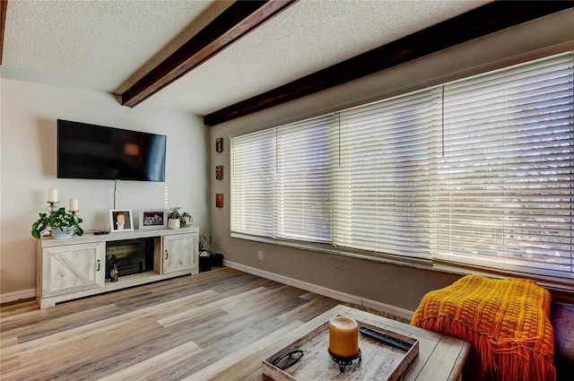 living room with a textured ceiling, light hardwood / wood-style floors, and beamed ceiling