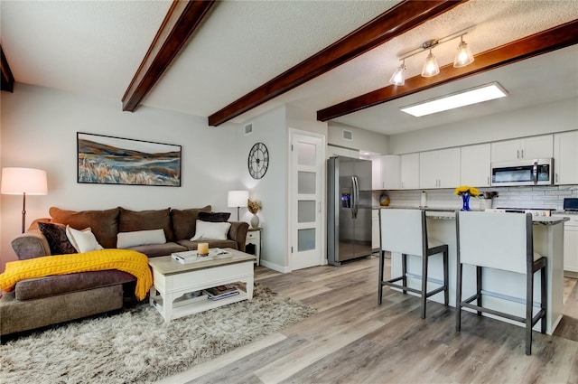 living room with a textured ceiling, light hardwood / wood-style flooring, and beamed ceiling