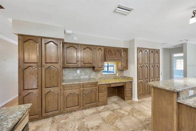 kitchen featuring tasteful backsplash, light stone countertops, and built in desk