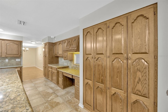 kitchen with light tile patterned flooring, built in desk, an inviting chandelier, and decorative backsplash