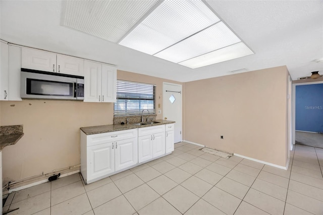 kitchen featuring dark stone countertops, sink, light tile patterned floors, and white cabinets