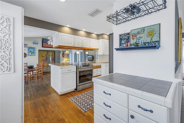 kitchen with white cabinetry, stainless steel electric range oven, tile countertops, light wood-type flooring, and kitchen peninsula