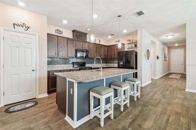 kitchen with dark brown cabinetry, decorative light fixtures, black appliances, and a center island with sink