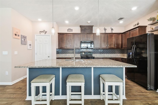 kitchen featuring pendant lighting, light stone countertops, black appliances, and a center island with sink