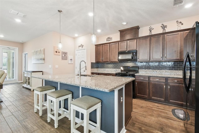 kitchen featuring sink, decorative light fixtures, black appliances, and an island with sink