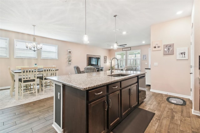 kitchen with hardwood / wood-style floors, sink, light stone counters, dark brown cabinetry, and a center island with sink