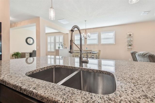 kitchen featuring sink, an inviting chandelier, light stone counters, a textured ceiling, and decorative light fixtures