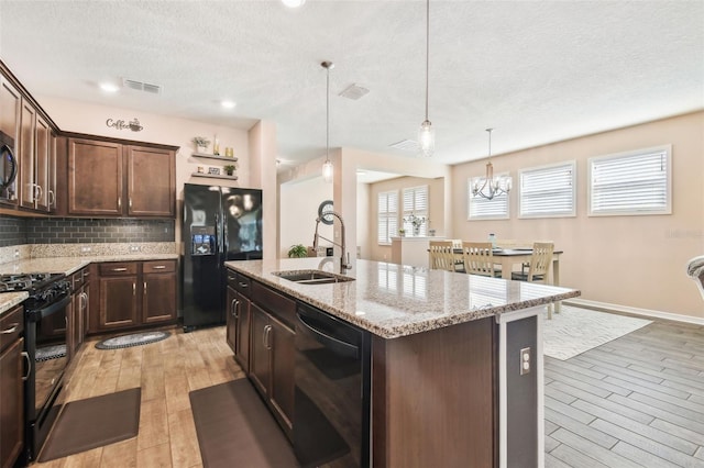 kitchen featuring decorative light fixtures, an island with sink, sink, black appliances, and dark brown cabinets