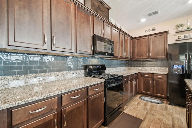 kitchen with dark brown cabinetry, light stone counters, black appliances, light hardwood / wood-style flooring, and backsplash