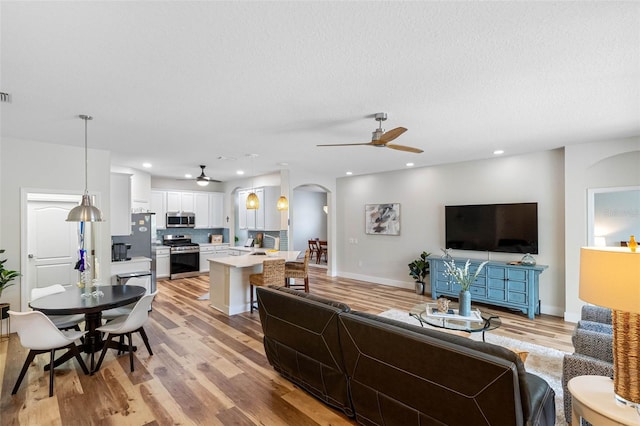 living room featuring ceiling fan, a textured ceiling, and light wood-type flooring