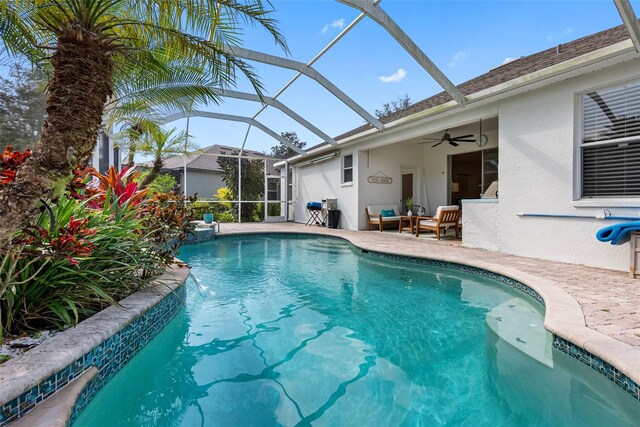 view of swimming pool with pool water feature, glass enclosure, ceiling fan, an outdoor living space, and a patio