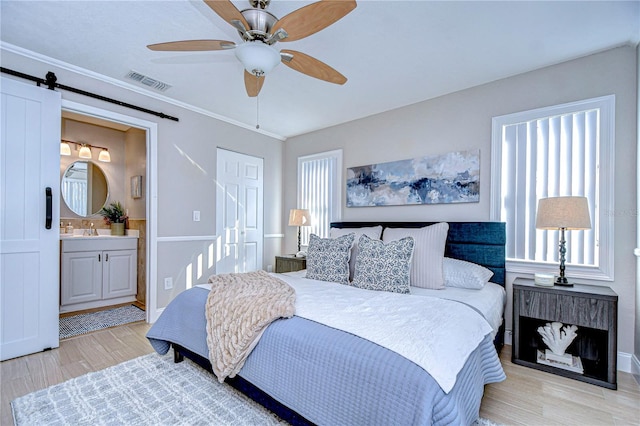 bedroom with multiple windows, sink, light hardwood / wood-style floors, and a barn door